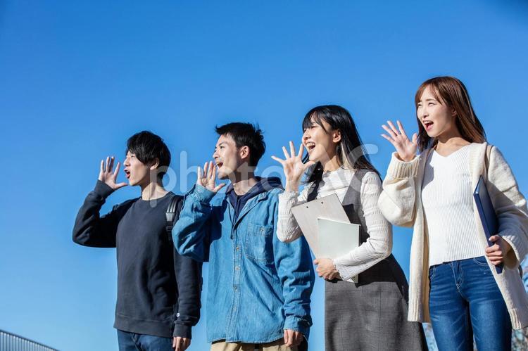 青空の下で声を上げる4人の学生（PhotoACサンプル）